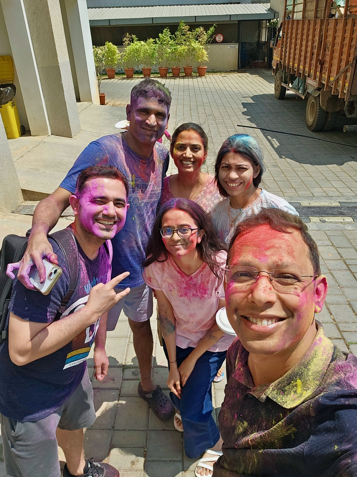 Teammates covered in colour, crowded into a selfie during a Holi celebration.