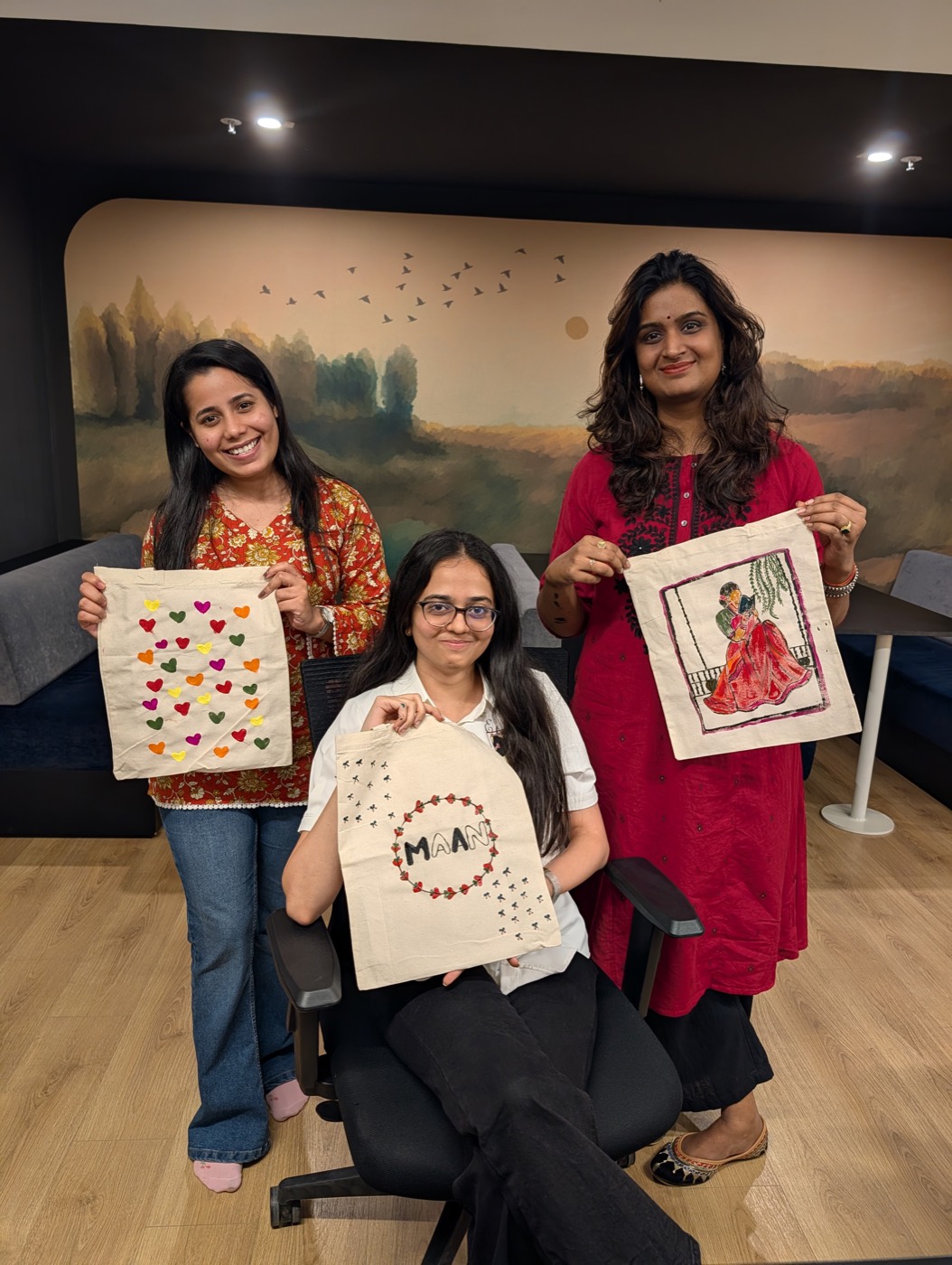 Three teammates holding up canvases they painted during a relaxed craft session.