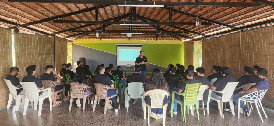 A working session at the offsite: the team seated in a thatched open hall, one person presenting at a screen